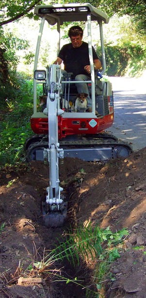 Photo of Graham Howard at the controls of his mini digger doing some pipe and cable laying with his two Jack Russell Terriers